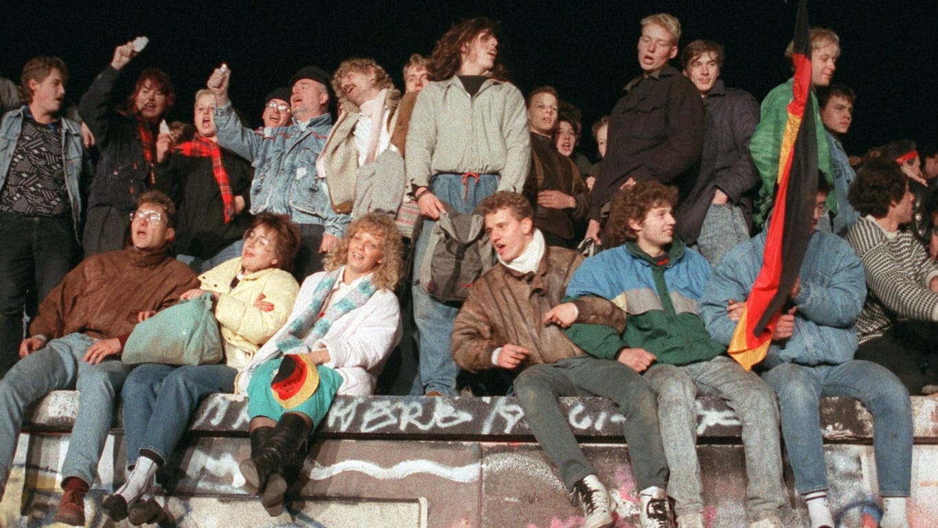 Singend und schunkelnd freuen sich junge Menschen am 10.11.1989 auf der Berliner Mauer über die Grenzöffnung: Schon damals wurde aus "Wir sind das Volk" schnell "Wir sind ein Volk".