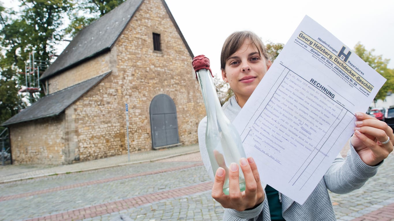 Vanessa Nöhr von der Stadt Goslar zeigt eine alte Flaschenpost sowie eine Kopie des darin gefundenen Schreibens vor der Domvorhalle: Dachdecker hatten die Flasche im Jahr 1930 mit einer Botschaft für die Nachwelt versehen, sie dann aber nicht irgendwo ins Wasser geworfen, sondern unter dem Dach der Domvorhalle versteckt. Dort wurde sie jetzt gefunden.