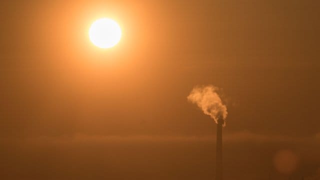 Durch einen Dunstschleier scheint die aufgehende Sonne einen Schornstein an, der seinen Dampf in die Atmosphäre entlässt. Durch einen Dunstschleier scheint die aufgehende Sonne einen Schornstein an, der seinen Dampf in die Atmosphäre entlässt.