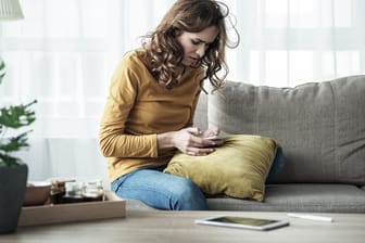 Eine Frau auf dem Sofa blickt besorgt auf ihr Smartphone: Wenn die WLAN-Verbindung im Heimnetzwerk häufig zusammenbricht, liegt der Grund vielleicht im Mauerwerk versteckt.