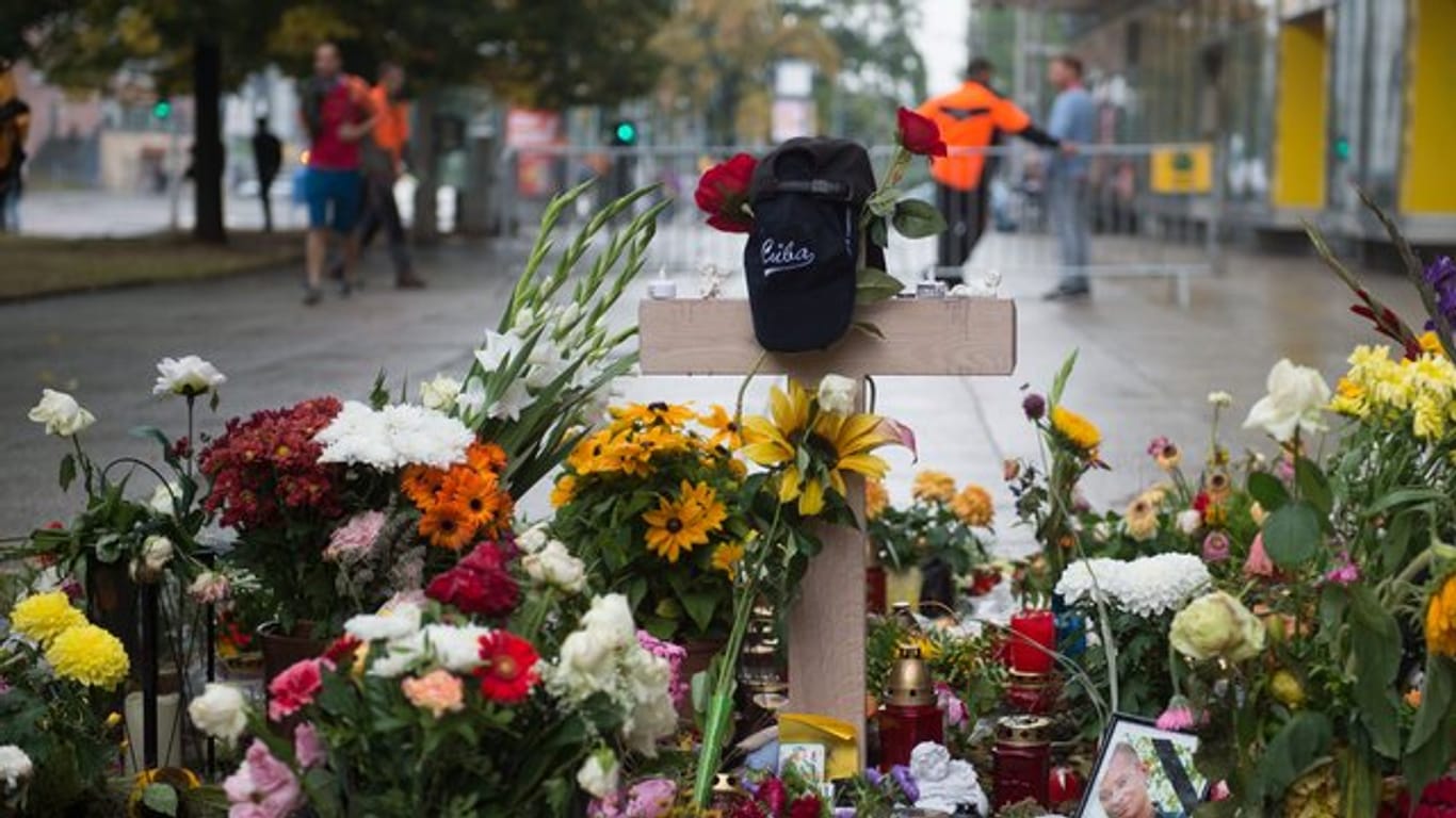 Ein Holzkreuz und zahlreiche Blumen und Kerzen stehen in Chemnitz am Tatort der Messerattacke.