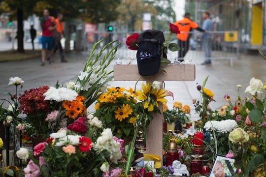 Ein Holzkreuz und zahlreiche Blumen und Kerzen stehen in Chemnitz am Tatort der Messerattacke.