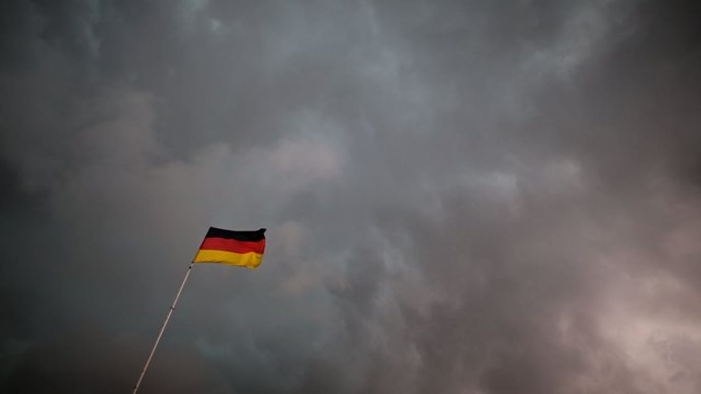 Eine Deutschlandfahne weht unter Gewitterwolken.