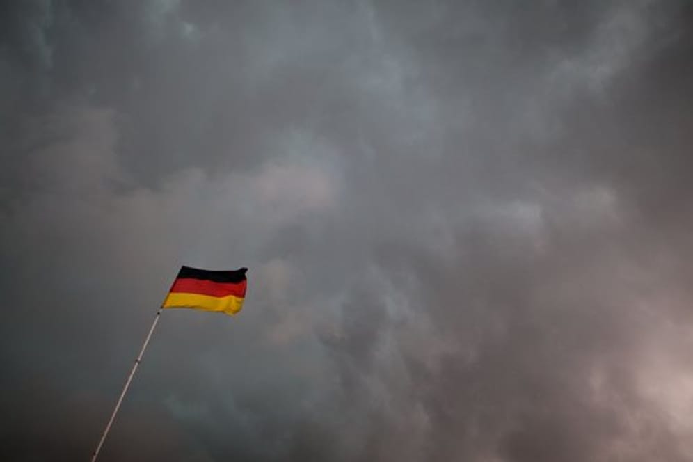 Eine Deutschlandfahne weht unter Gewitterwolken.