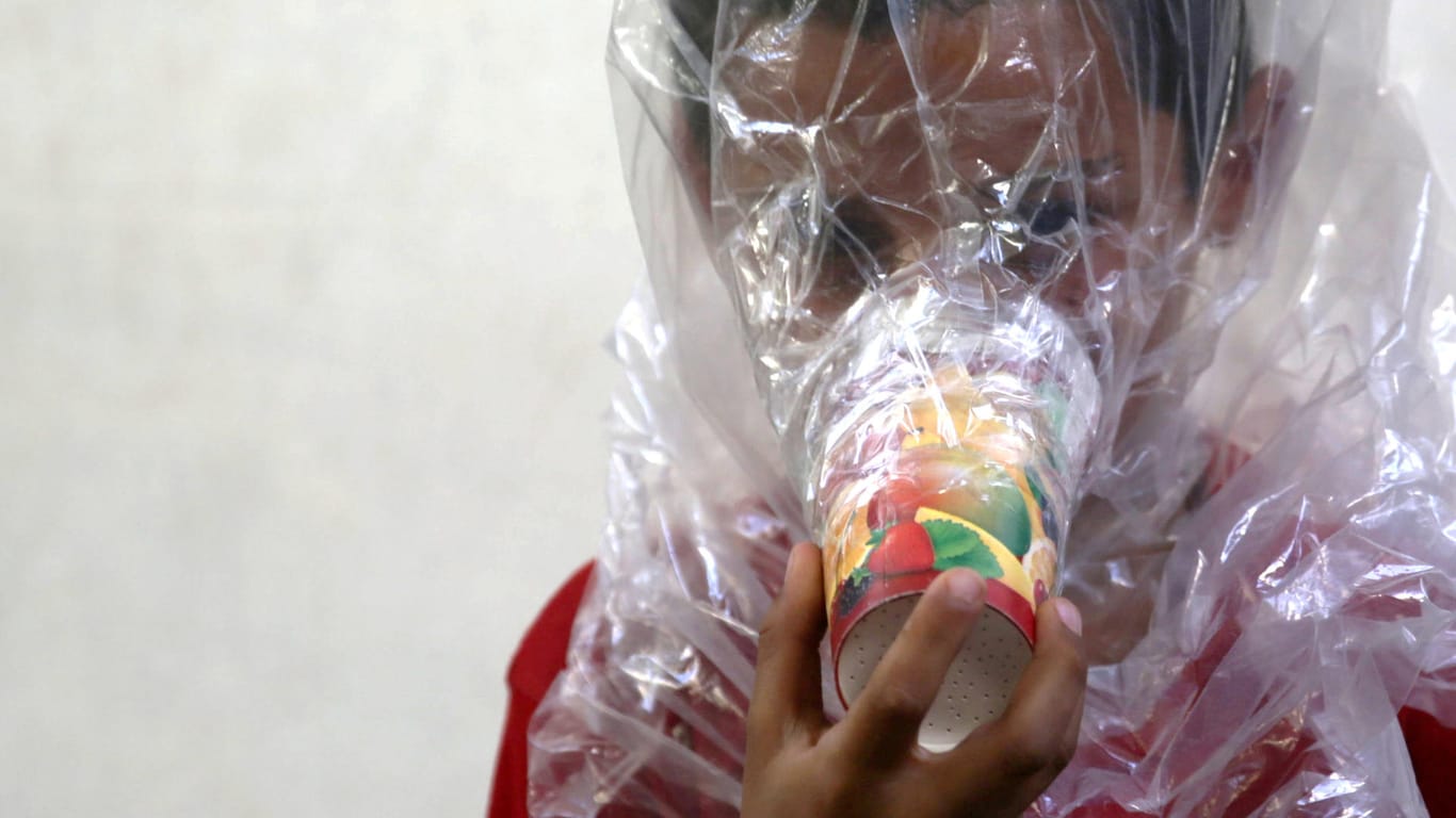 Vorbereitung für den Ernstfall: Ein Kind hält eine Gasmaske, gebastelt aus einer Plastiktüte und einem Becher, vors Gesicht.
