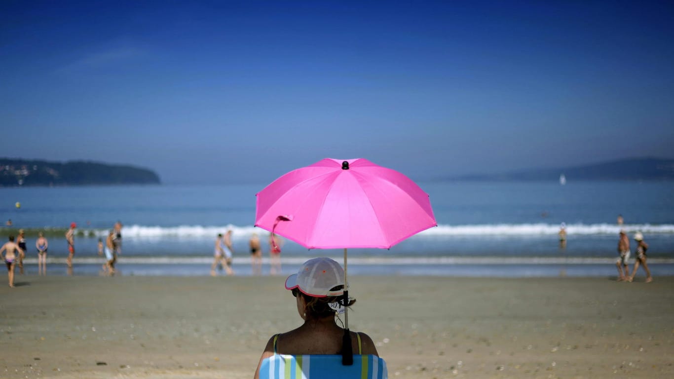 Eine Frau sitzt unter einem pinken Sonnenschirm: An vielen Stränden ist das Rauchen bereits verboten.