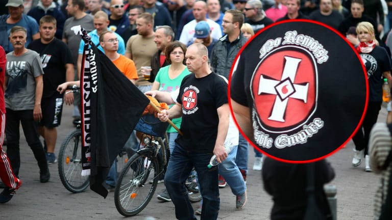 Ku-Klux-Klan-Symbol: Ein Mann trug beim "Trauermarsch" ein Shirt mit dem "Blood-Drop Cross“. Das Blutstropfen-Kreuz soll für Jesus stehen, der nach der Ideologie des Klans ("Invisible Empire", unsichtbares Imperium) nur für die weiße Rasse gestorben sei. Das Shirt ist ein Fanartikel der britischen Neonazi-Band "No Remorse", die zu den Gründern des seit 2000 in Deutschland verbotenen "Blood & Honour"-Netzwerks gehörte. Verboten sind der KKK und seine Symbole in Deutschland nicht.