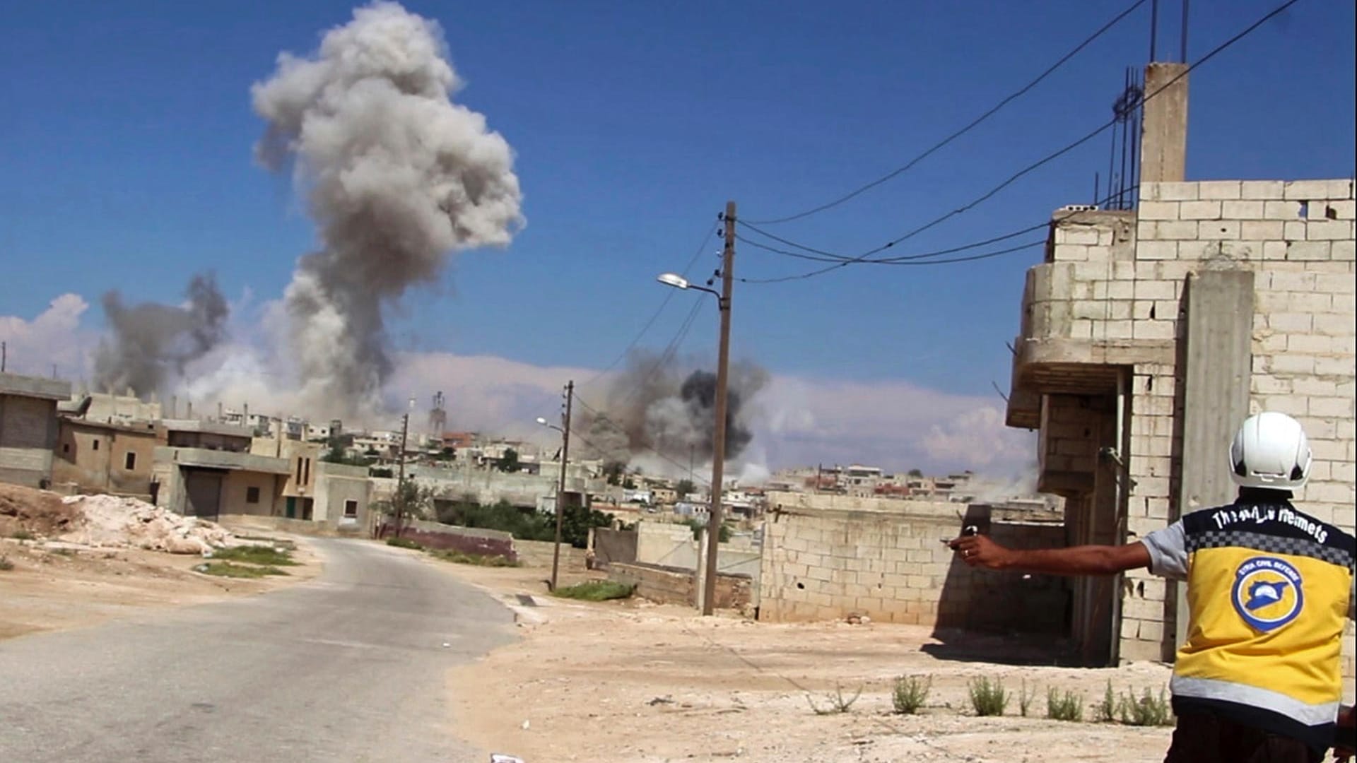 Ein syrischer Weißhelm, im Hintergrund Rauch, der nach einem Luftangriff auf Hobeit bei Idlib aufsteigt: Die Mitarbeiter der Organisation helfen nach Angriffen den Opfern.