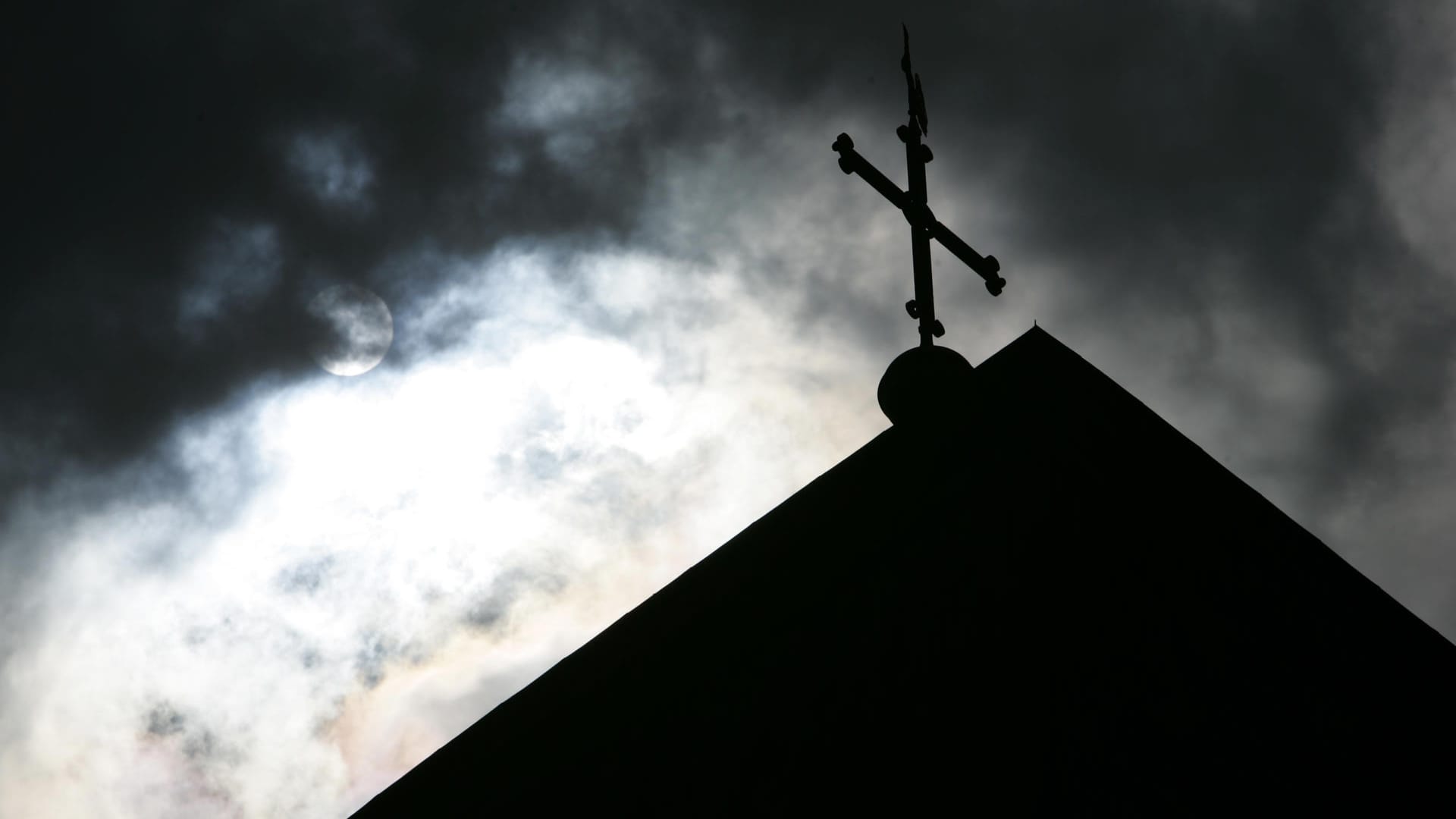 Eine Kirchturmspitze vor einem wolkenverhangenen Himmel (Symbolbild): Eine Studie dokumentiert Missbrauch in der katholischen Kirche in Deutschland.