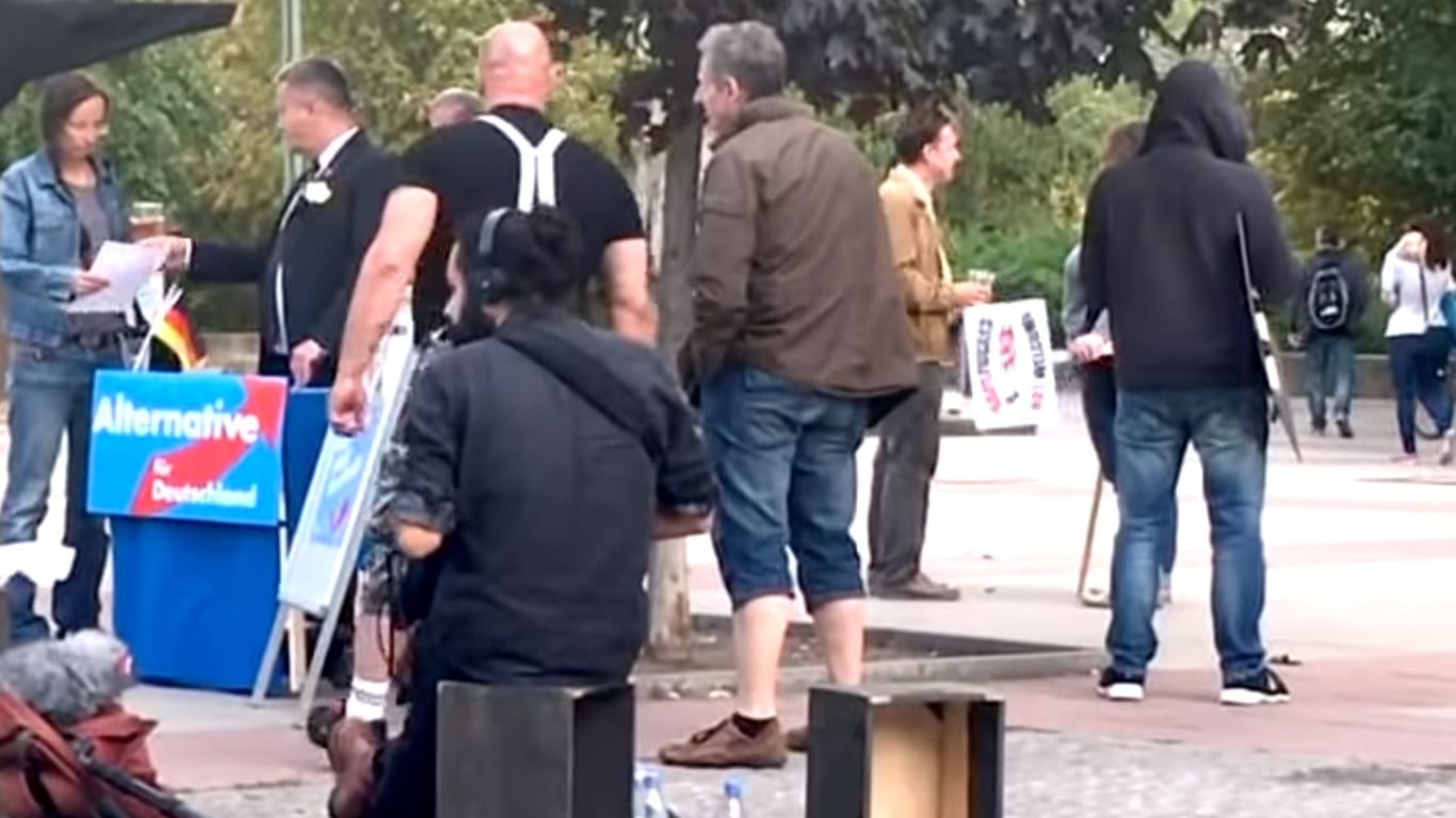 Szene im Berliner Stadtteil Lichtenberg: An einem Stand mit einem verfremdeten AfD-Logo steht ein Schauspieler im Skinhead-Look, drumherum laufen Mitarbeiter der Produktionsfirma. Das ist ein Screenshot aus dem Beitrag, in dem die AfD sich über ein "Fake" empört.