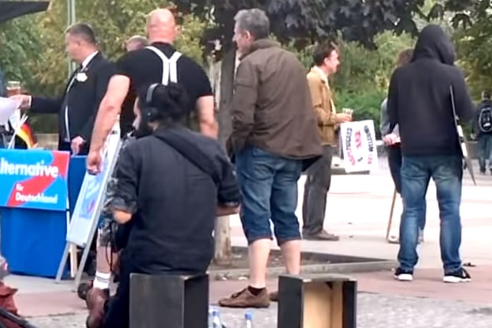 Szene im Berliner Stadtteil Lichtenberg: An einem Stand mit einem verfremdeten AfD-Logo steht ein Schauspieler im Skinhead-Look, drumherum laufen Mitarbeiter der Produktionsfirma. Das ist ein Screenshot aus dem Beitrag, in dem die AfD sich über ein "Fake" empört.