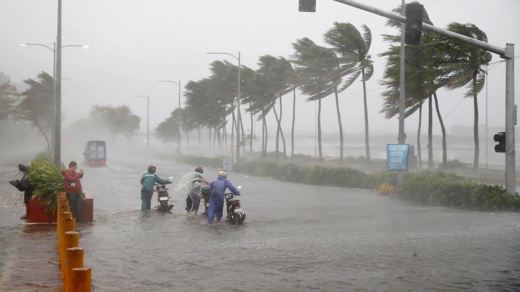 Verkehrsteilnehmer schieben während heftiger Regenfälle und starken Winden, die durch den Taifun "Mangkhut" verursacht wurden, ihre Motorroller über eine überflutete Straße. Verkehrsteilnehmer schieben während heftiger Regenfälle und starken Winden, die durch den Taifun "Mangkhut" verursacht wurden, ihre Motorroller über eine überflutete Straße.