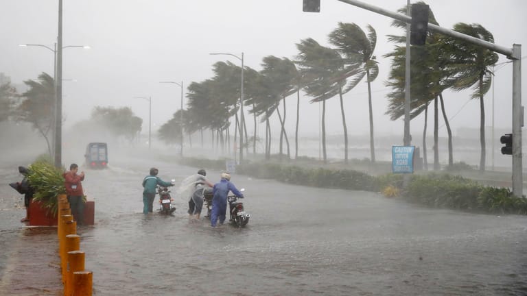Verkehrsteilnehmer schieben während heftiger Regenfälle und starken Winden, die durch den Taifun "Mangkhut" verursacht wurden, ihre Motorroller über eine überflutete Straße.