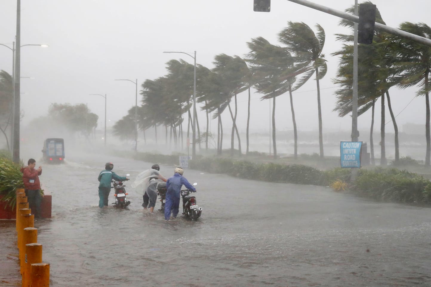 Verkehrsteilnehmer schieben während heftiger Regenfälle und starken Winden, die durch den Taifun "Mangkhut" verursacht wurden, ihre Motorroller über eine überflutete Straße.