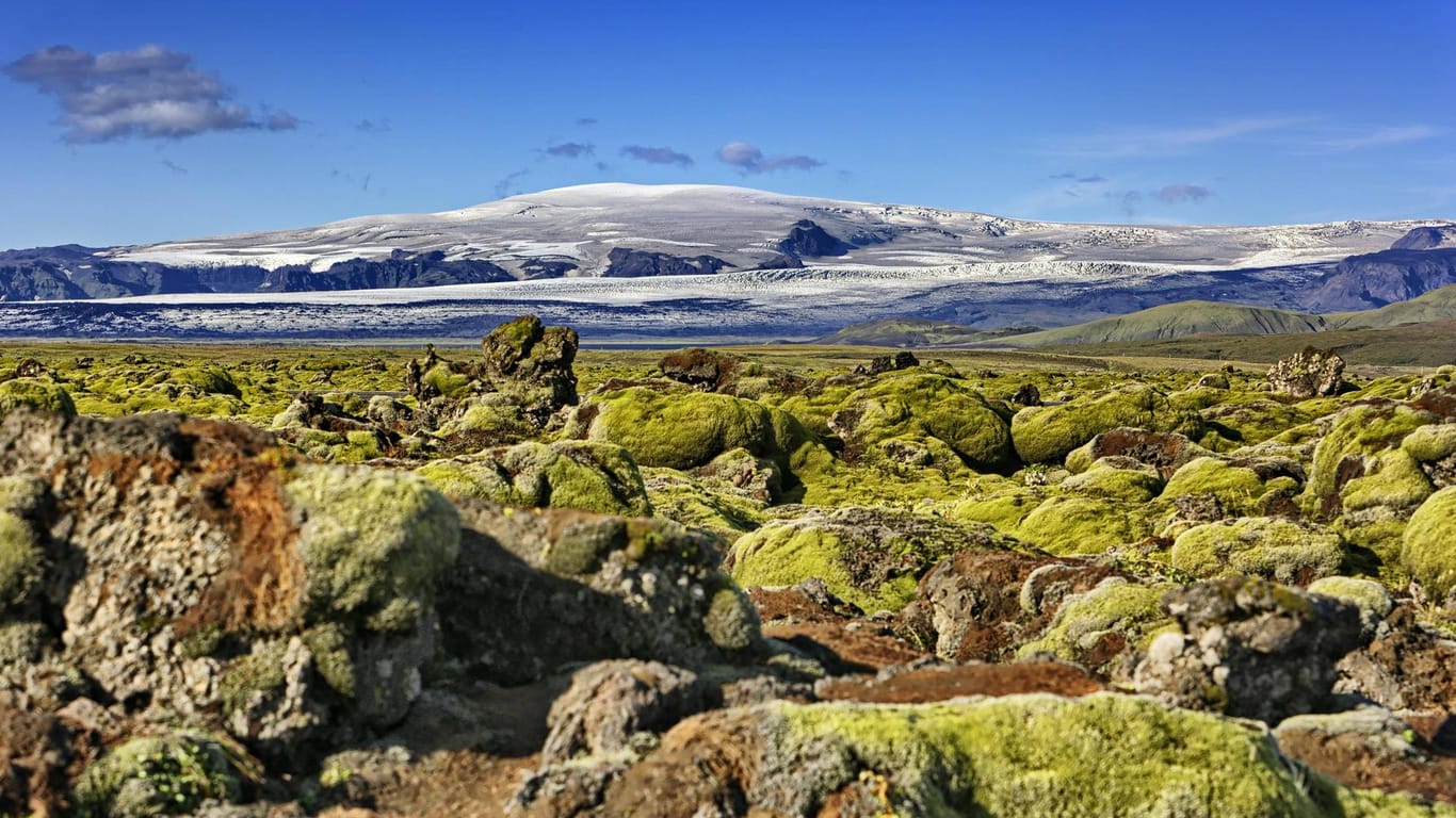 Ein mit Moos bewachsenes Lavafeld mit dem Vulkan Katla im Hintergrund (Archivbild): Neue Messverfahren zeigen, dass der Vulkan in Island große Mengen an CO2 ausstößt. Diese seien ein deutlicher Hinweis auf bedeutende Aktivitäten innerhalb des Vulkans, so eine Vulkanologin der britischen Universität Leeds.
