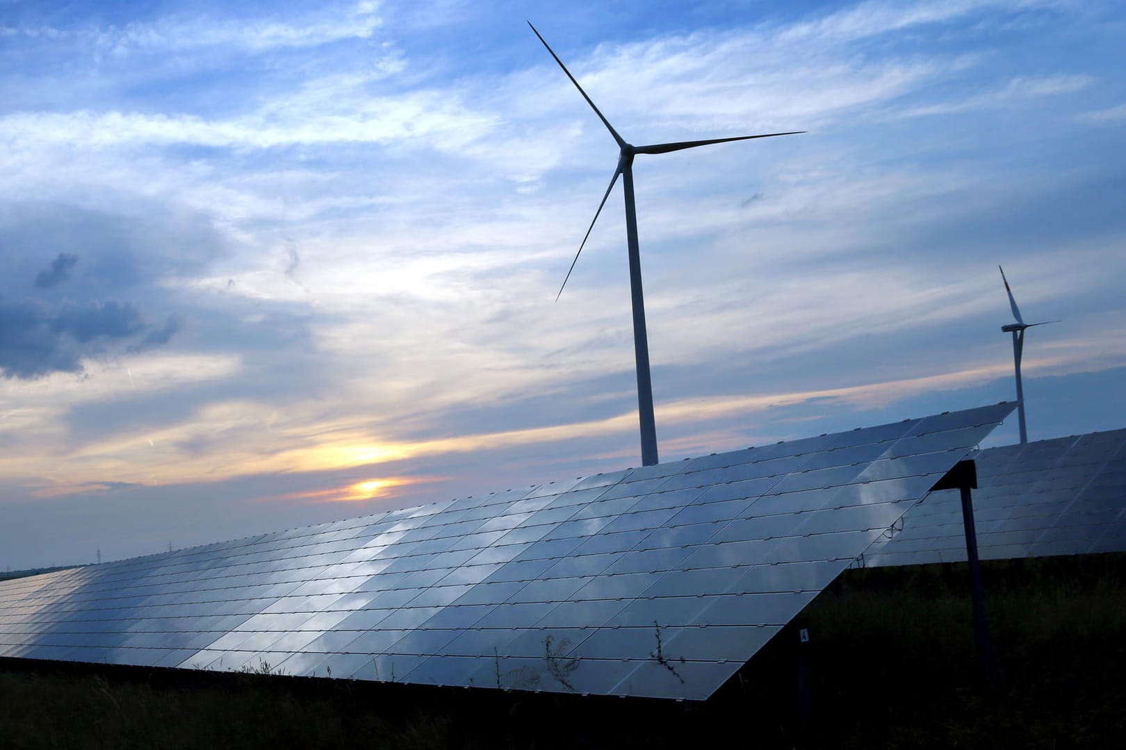 Solarzellen einer Solarkraftanlage vor Windrädern: Bis 2050 soll laut einer norwegischen Studie die Hälfte der Energie weltweit aus erneuerbaren Quellen stammen.
