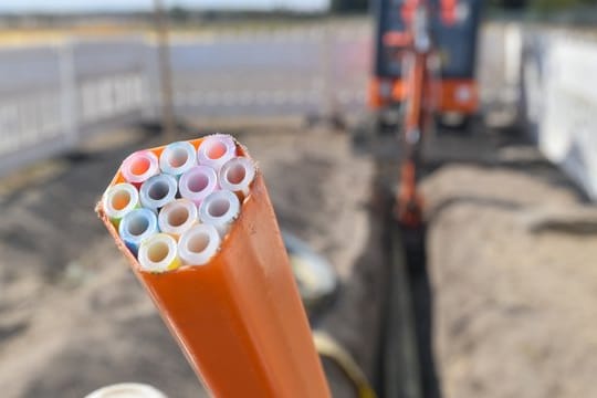 Farbige Leerrohre, in die später die Glasfaserkabel verlegt werden, ragen aus einem Graben auf einer Baustelle im brandeburgischen Grassau.