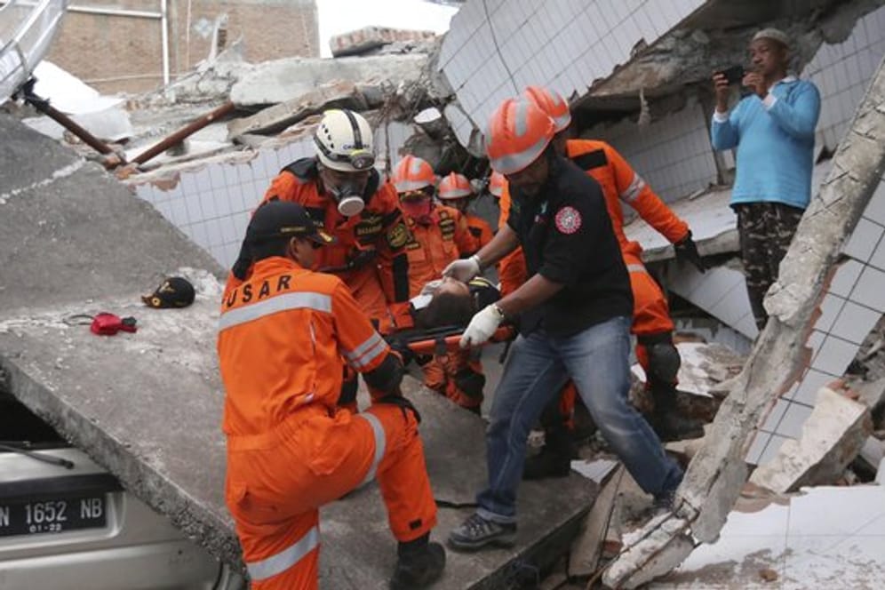 Rettungskräfte tragen einen Verletzten aus den Trümmern eines Restaurants, das durch das Erdbeben und den darauf folgenden Tsunami zerstört wurde.