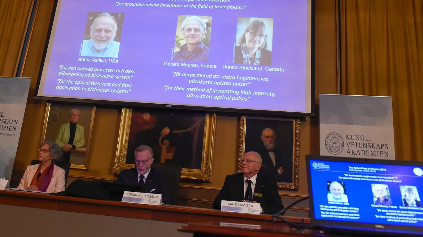 Schweden, Stockholm: Die Nobelpreisträger für Physik 2018, Arthur Ashkin aus den USA (von links nach rechts), Gerard Mourou aus Frankreich und Donna Strickland aus Kanada, sind auf einem Bildschirm während der Verkündung in der Königlich Schwedischen Akademie der Wissenschaften zu sehen.