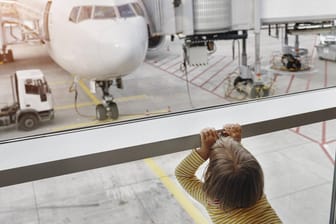 Ein kleines Mädchen schaut durch ein Fenster auf ein Flugzeug: In Stuttgart vergaßen Eltern ihre fünfjährige Tochter am Flughafen.