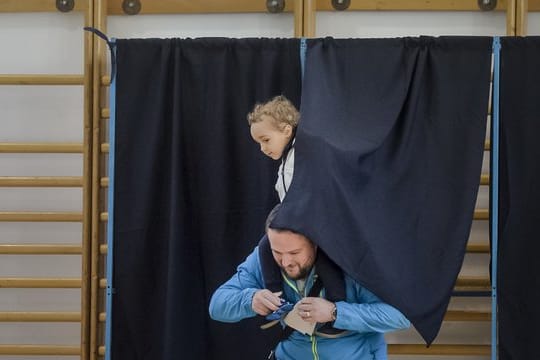 Ein Mann verlässt mit einem Kind auf seinen Schultern eine Wahlkabine.