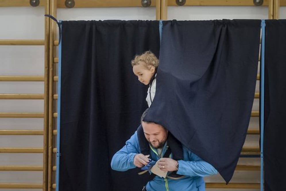 Ein Mann verlässt mit einem Kind auf seinen Schultern eine Wahlkabine.