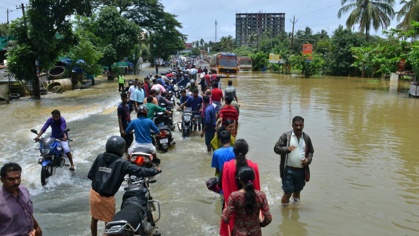 Menschen überqueren eine überflutete Straße in Indien: Der globale Meeresspiegel würde bis zum Ende dieses Jahrhunderts bei 1,5 Grad Erwärmung um 10 Zentimeter weniger klettern als bei 2 Grad.