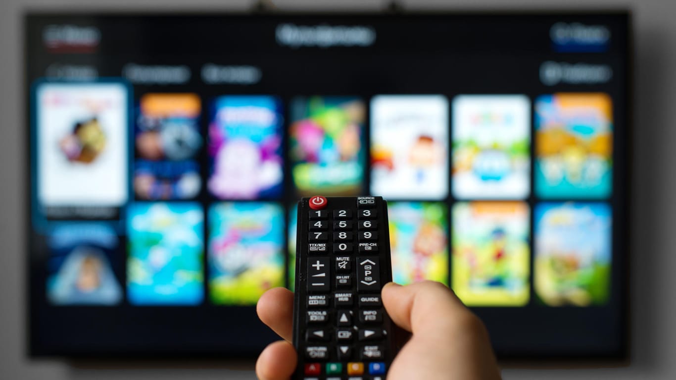 Hand mit Fernbedienung vor Fernseher: Das Bundesamt für Sicherheit in der Informationstechnik empfiehlt, HbbTV zu deaktivieren, wenn es nicht genutzt wird.