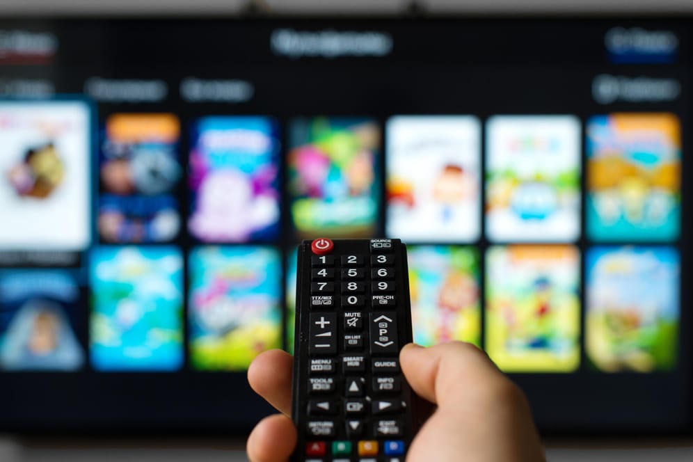 Hand mit Fernbedienung vor Fernseher: Das Bundesamt für Sicherheit in der Informationstechnik empfiehlt, HbbTV zu deaktivieren, wenn es nicht genutzt wird.