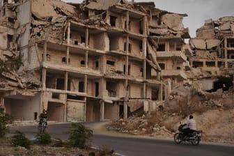 Motorräder fahren an Gebäuden vorbei, die im Zuge der Kämpfe in der Provinz Idlib zerstört wurden.