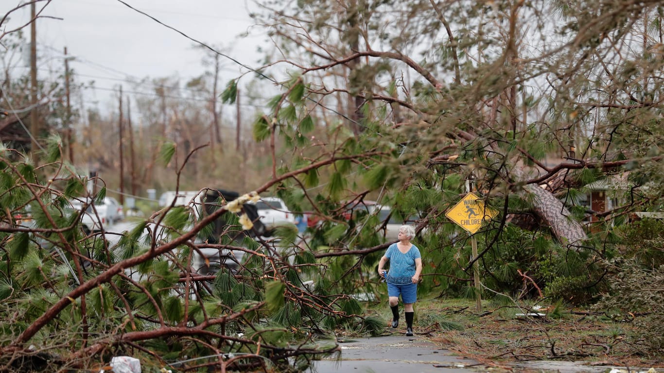 Ein Anwohnerin geht zwischen umgeknickten Bäumen durch ihre Nachbarschaft: Behörden haben Such- und Rettungsmannschaften in die besonders schlimm getroffenen Gebiete geschickt.