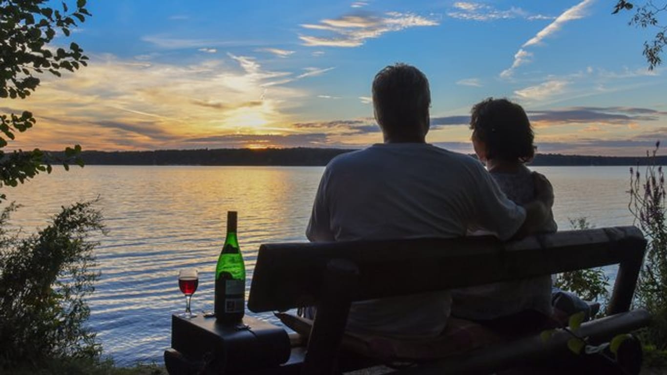 Mit einer Flasche Rotwein genießt ein Pärchen den Sonnenuntergang am See.