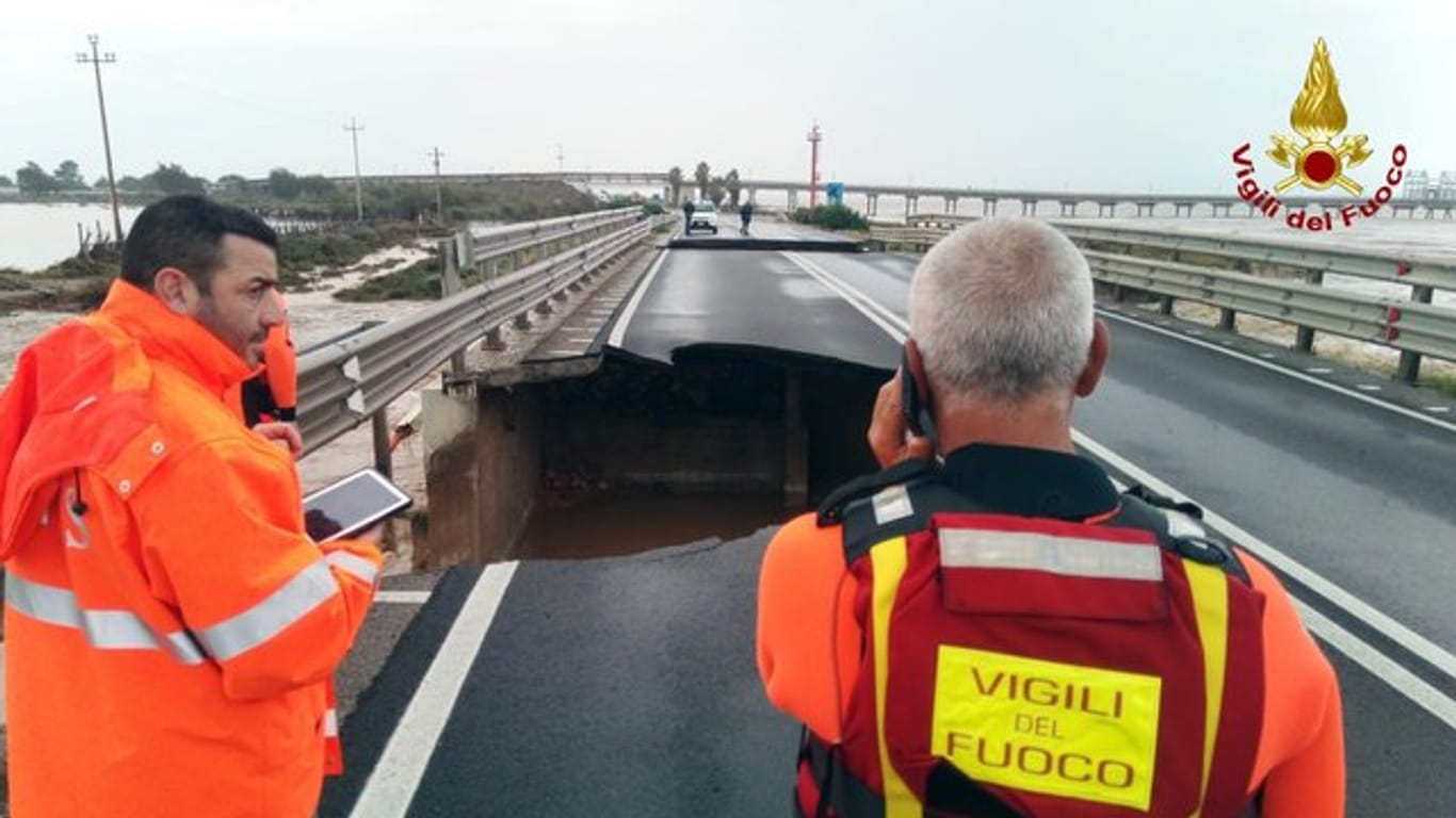Feuerwehrleute stehen neben der beschädigten Brücke über den Fluss Santa Lucia an der Straße von Cagliari nach Capoterra.