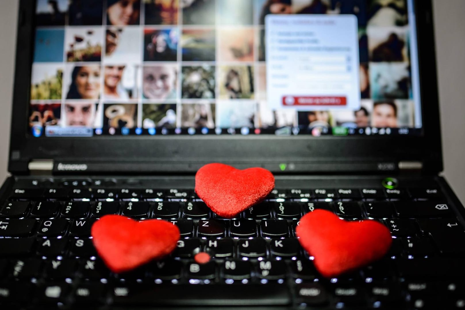Deko-Herzchen liegen auf einer Laptop-Tastatur: Auf vielen Dating-Portalen tummeln sich auch Betrüger.
