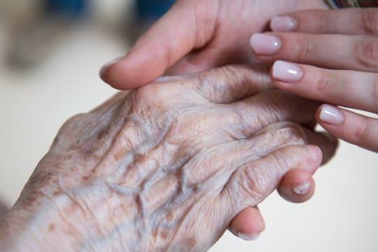 Eine Pflegerin hält die Hand einer älteren Dame.