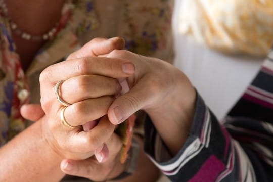 Eine Therapeutin hält in einem Hospiz in Stuttgart die Hand einer todkranken Bewohnerin.