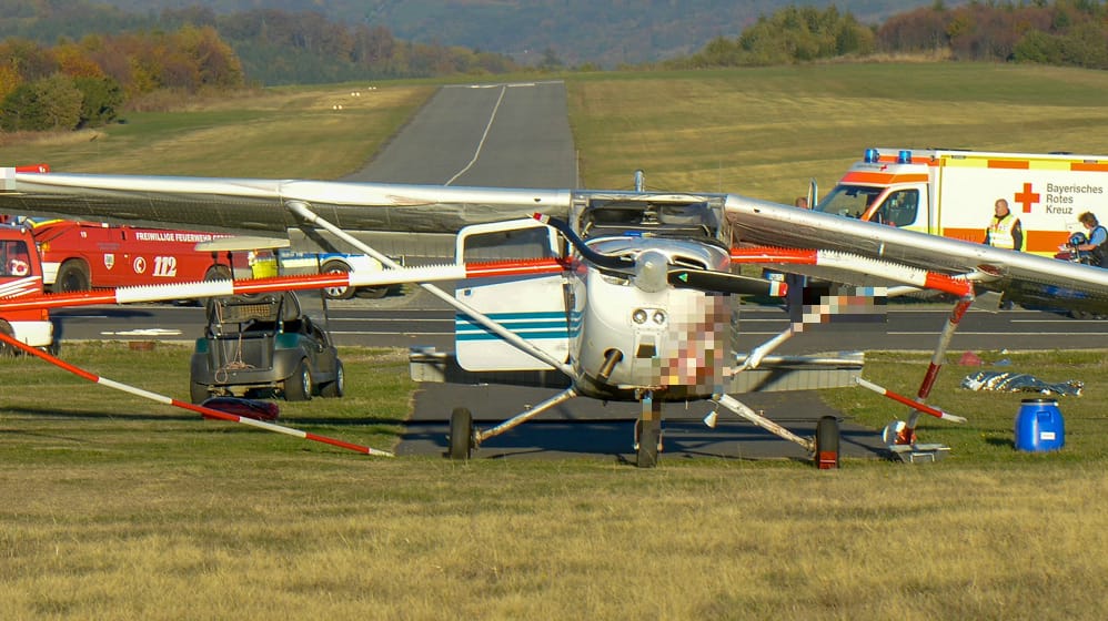 Gersfeld: Feuerwehrleute stehen nach einem Flugunfall neben einem Sportflugzeug. Das Kleinflugzeug hatte bei einer missglückten Landung auf Hessens höchstem Berg am Nachmittag eine Absperrung des Flugplatzes durchbrochen und Passanten auf einem Gehweg erfasst.