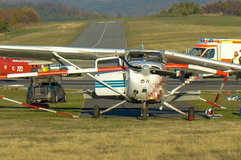 Gersfeld: Feuerwehrleute stehen nach einem Flugunfall neben einem Sportflugzeug. Das Kleinflugzeug hatte bei einer missglückten Landung auf Hessens höchstem Berg am Nachmittag eine Absperrung des Flugplatzes durchbrochen und Passanten auf einem Gehweg erfasst.