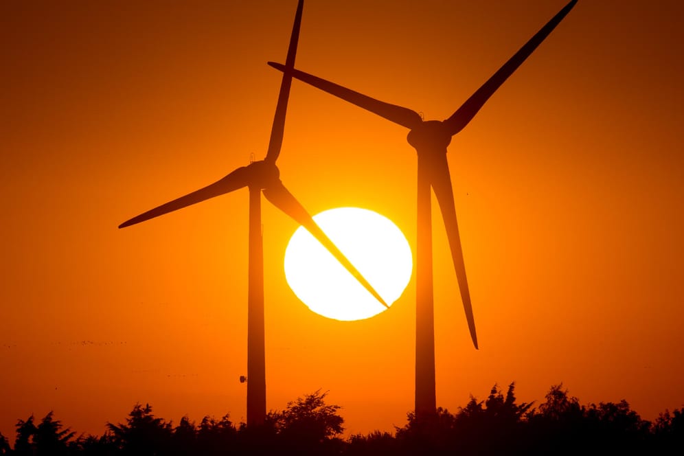 Sonne geht hinter zwei Windrädern unter: Die EEG-Umlage finanziert die festen Vergütungen, die Ökostrom-Produzenten für ihren Strom bislang unabhängig vom Marktpreis bekommen.