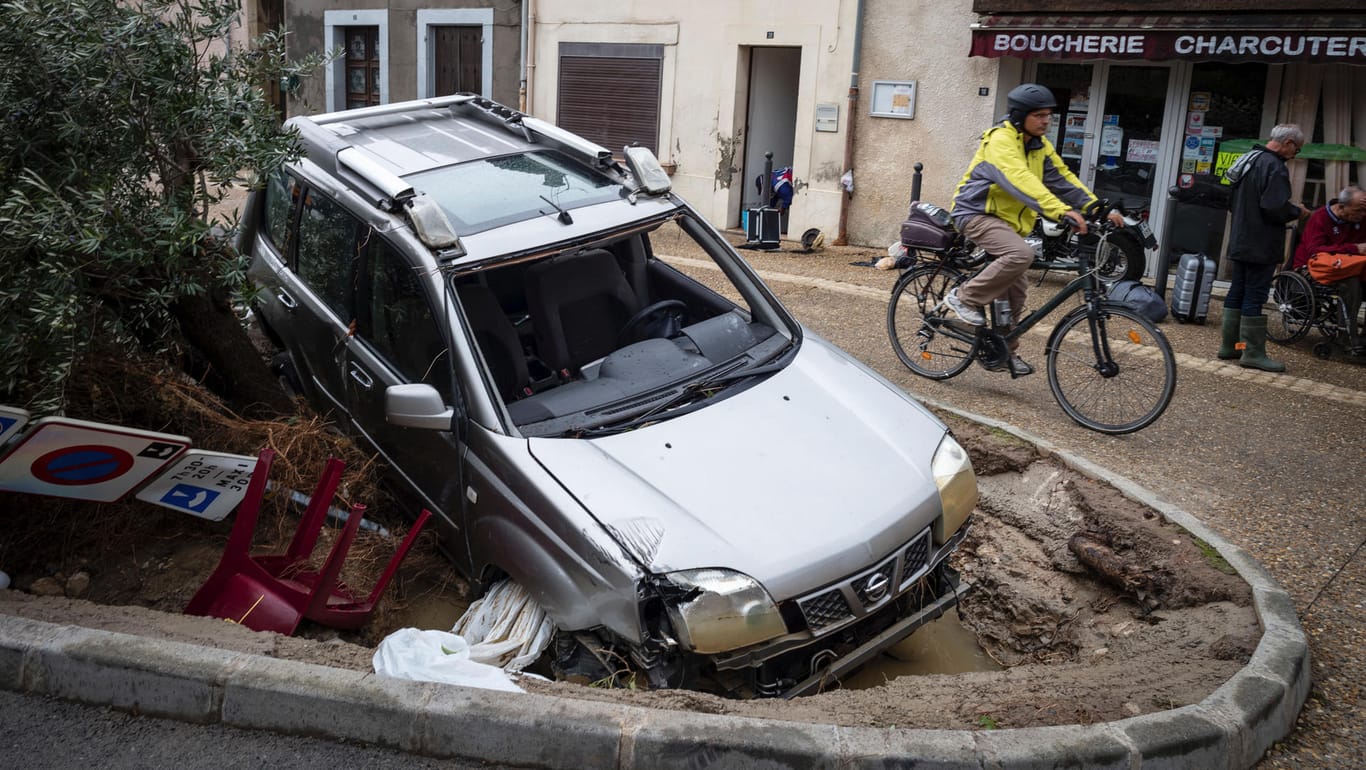 Frankreich, Villegailhenc: Ein Radfahrer fährt an einem von den Fluten demolierten Auto vorbei. Bei Überschwemmungen im Süden Frankreichs sind einige Menschen ums Leben gekommen.