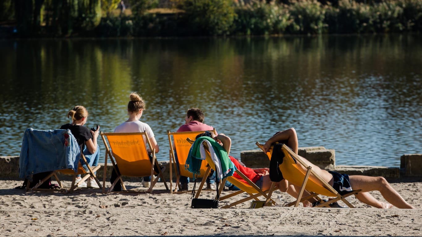 Sonnenbadende in Stuttgart: Bei sommerlichen Temperaturen entspannen sich am Max-Eyth-See einige junge Leute an einem kleinen Strand.