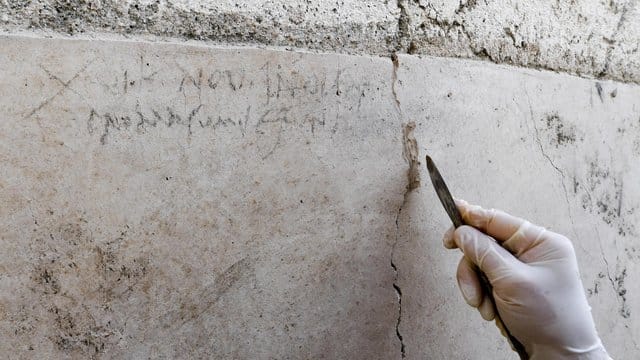 Ein Archäologe zeigt an einer Mauer in Pompeji die Kohle-Inschrift, die auf die Eruption des Vesuv im Jahr 79 verweist. Ein Archäologe zeigt an einer Mauer in Pompeji die Kohle-Inschrift, die auf die Eruption des Vesuv im Jahr 79 verweist.