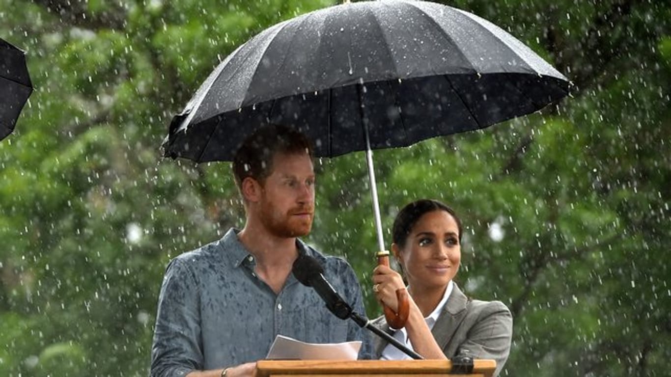 Prinz Harry neben Herzogin Meghan, die während eines Regenschauers einen Schirm hält, in Gubbo.