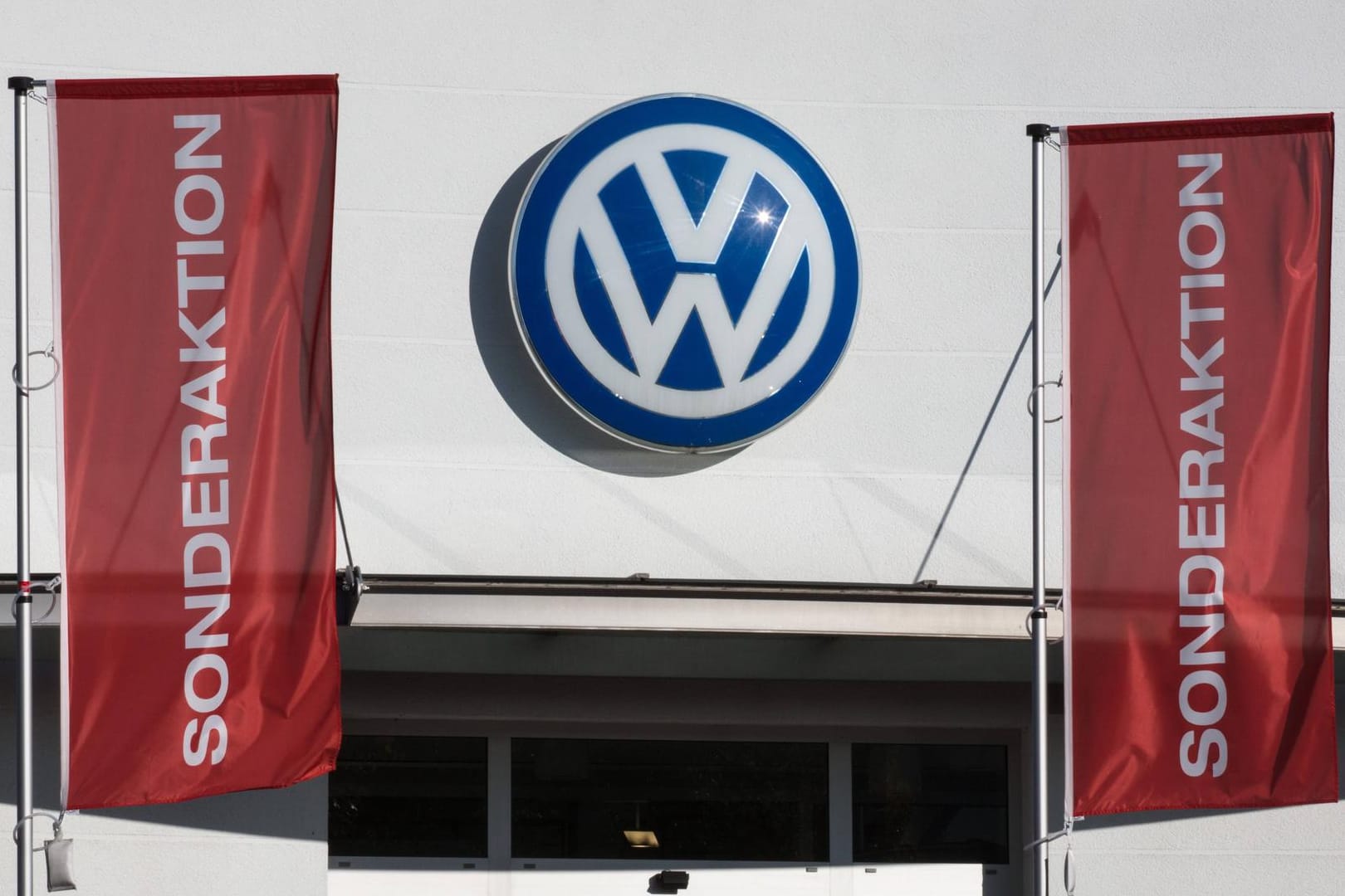 Fahnen mit der Aufschrift Sonderaktion hängen an einem Volkswagen-Autohaus vor einer Fassade mit VW-Emblem