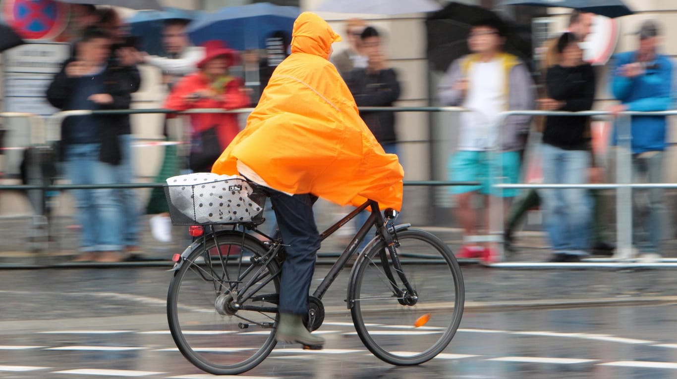 Eine Radfahrerin schützt sich mit einem Cape vor Regen: Das kommende Wetter wird herbstlich und regnerisch.