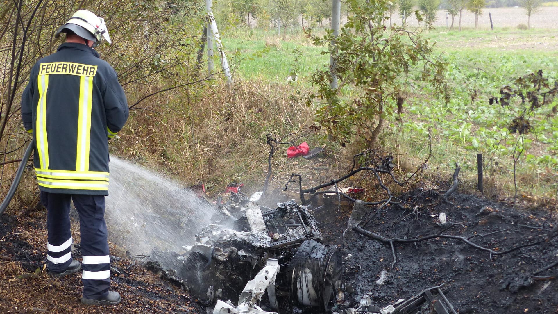 Ein Feuerwehrmann löscht die Überreste eines ausgebrannten Ferrari: Zwei Männer verbrannten in dem Auto. Ein Feuerwehrmann löscht die Überreste eines ausgebrannten Ferrari: Zwei Männer verbrannten in dem Auto.