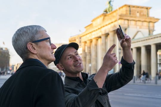 Apple-Chef Tim Cook (l) lässt sich am Brandenburger Tor von Entwickler Peter Kolski das Projekt "MauAR" erklären.