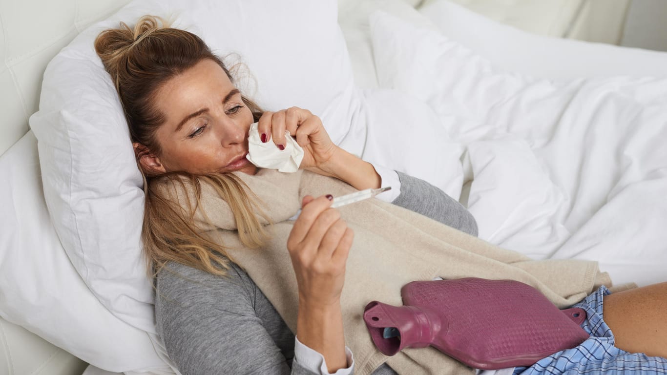 Eine kranke Frau im Bett misst Fieber.