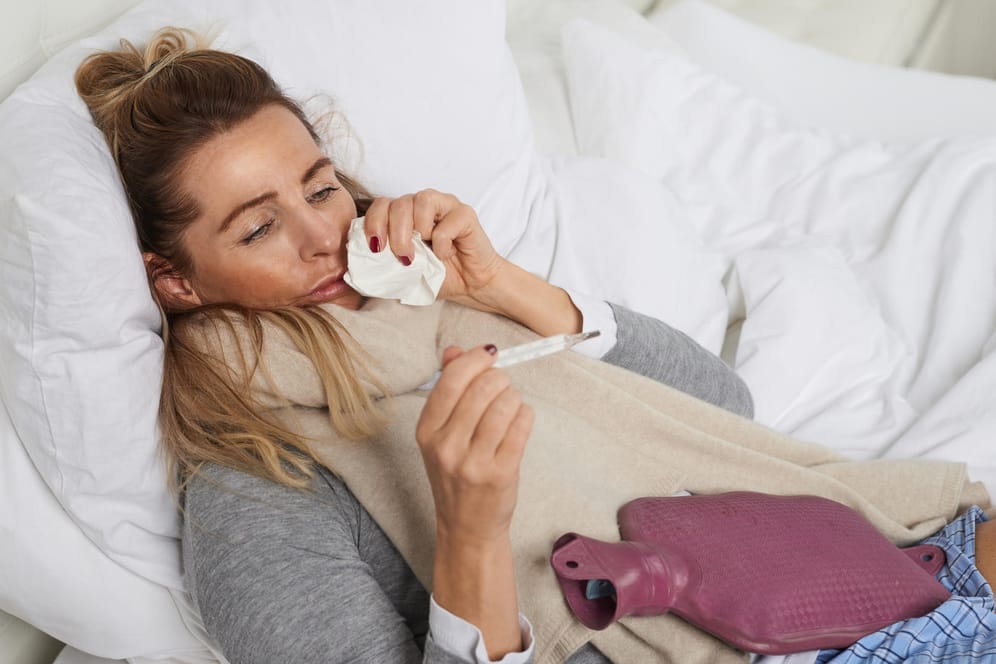 Eine kranke Frau im Bett misst Fieber.