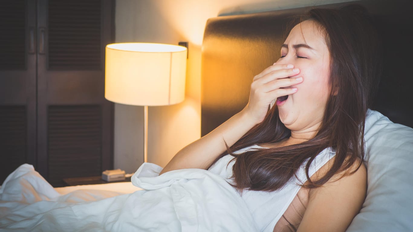 Eine junge Frau sitzt gähnend im Bett: Mit einer Tageslichtlampe lässt sich die Herbstmüdigkeit bekämpfen.